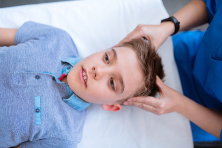 Being relaxed. Pleasant cute young boy peacefully lying on the couch during massage of his headの写真素材