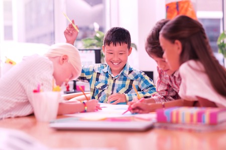 Dream team. Happily smiling boy sitting among his friends while drawing their school project together.の写真素材