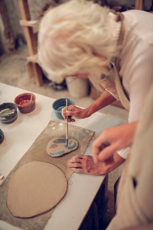 Careful process. Nice grey haired woman leaning forward while looking at her painting