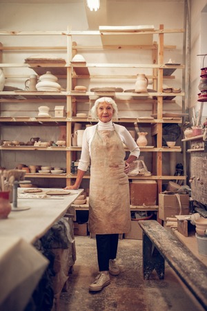 Small workshop. Joyful aged woman smiling while having her own businessの写真素材
