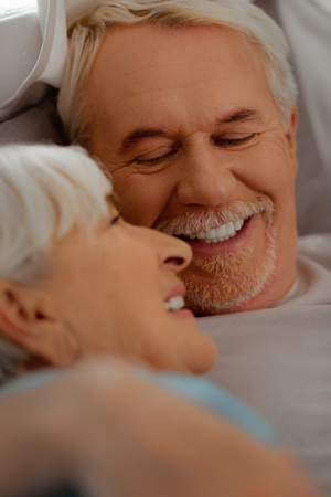 Loving look. Face-portrait of attractive white-haired vigorous bearded man in white t-shirt happily looking at his aging silver-haired beautiful wifeの写真素材