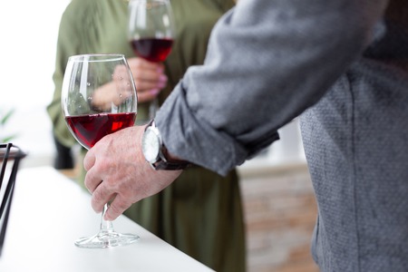 A glass with red wine. Close-up shot of male hand with watch on a wrist holding a glass of red wine standing on the table.の写真素材