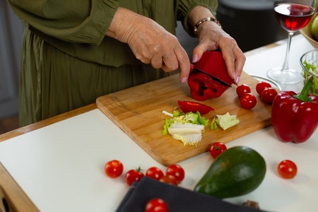 Cutting vegetables. Close-up shot of nice-looking cheerful talented energetic aged female wearing elegant green dress cutting vegetables for the romantic dinnerの写真素材