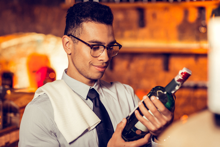 French wine. Dark-haired prosperous man wearing glasses looking at bottle of French wineの写真素材