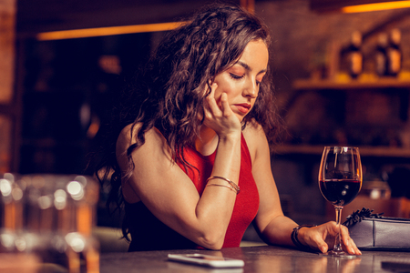 Sitting alone. Beautiful woman with natural makeup feeling bad sitting alone in the bar and drinking wineの写真素材