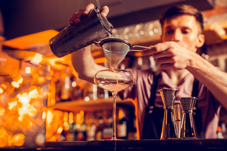 Bartender using sieve. Dark-haired bartender using sieve while making cocktail while standing at the bar standの写真素材