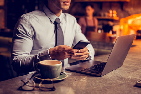 Texting friend. Businessman wearing tie sitting in the bar and texting friend after working on laptopの写真素材