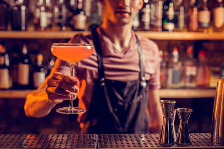 Nice alcohol cocktail. Professional barman wearing black apron showing nice alcohol cocktailの写真素材