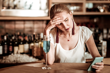 So stressed. Negative delighted blonde bowing her head while staring at screen of her gadgetの写真素材