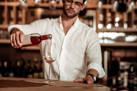 Small business. Concentrated bartender looking forward while pouring down wine into glassの写真素材