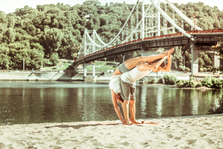 Partner acrobatics. Young sporty couple doing their stretching workout on the beach at sunriseの写真素材