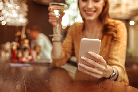 Holding a phone. Close-up photo of female hands holding a phone and clicking on it at the barの写真素材