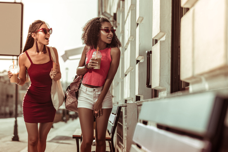 Strolling the streets. Stylish dark-haired tanned amazed appealing ladies walking the streets and looking at the windowsの写真素材