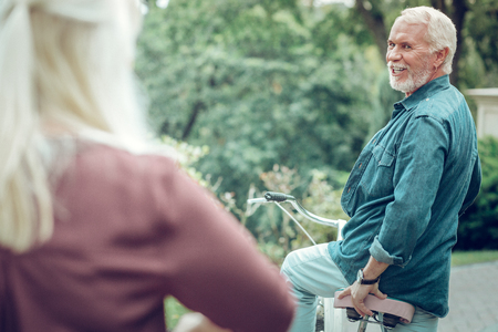 Having fun. Delighted bearded man turning to his wife while riding bikes together with herの写真素材