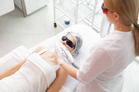 Beauty clinic. Nice blonde woman doing the laser procedure fir her client while working in the beauty clinicの写真素材