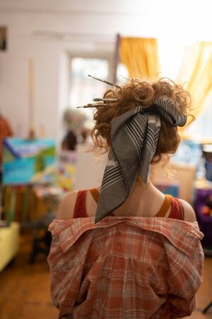 Brushes in her hair. Curly red-haired artist with hair bun having brushes in her hairの写真素材