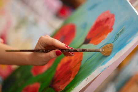 Painting poppies. Close up of artist with red nails holding painting brush and painting poppiesの写真素材