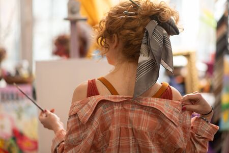 Cool hairstyle. Red-haired curly art student with cool hairstyle holding painting brushの写真素材