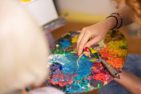 Gouache from palette. Top view of artist wearing bracelet taking gouache from color palette