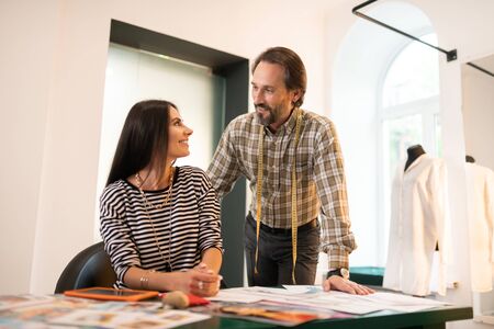 Fashion business. Appealing adult dark-haired handsome fashion designer talking to his business charming radiant alluring long-haired partner during work.の写真素材