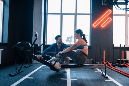 Trainer assisting woman. Bearded helpful trainer assisting woman with slight overweight in gymの写真素材