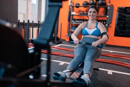 Woman with overweight. Dark-haired appealing woman with overweight smiling while working out in gym