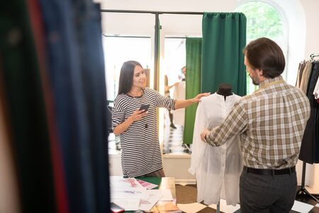 Partners during work. Good-looking talented fashion designer getting measurements of a white cotton...