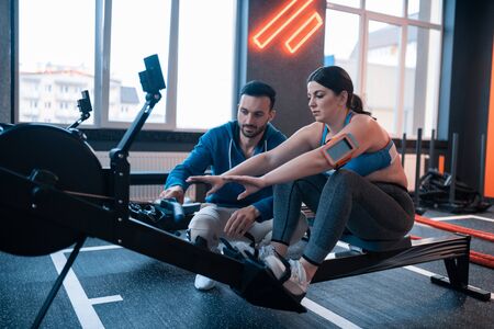 Trainer helping woman. Bearded dark-haired trainer helping woman with working out on exercise equipmentの写真素材