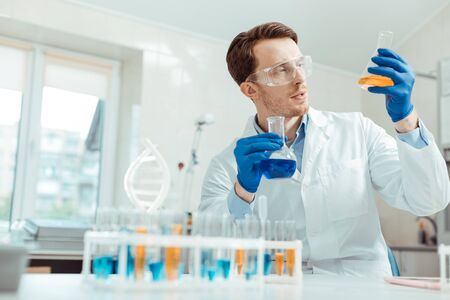 Professional chemist. Nice handsome man holding two different flasks while working in the chemical labの写真素材