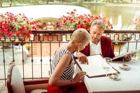 Looking at menu. Husband and wife looking at the menu while coming to restaurant and sitting at summer terraceの写真素材