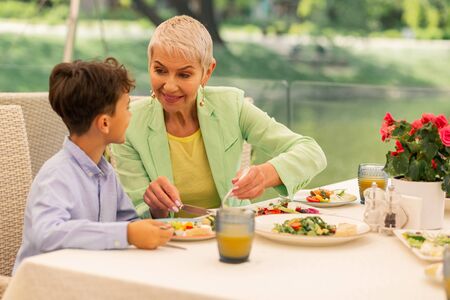 Beautiful grandmother. Loving beautiful grandmother smiling while giving her grandson some saladの写真素材