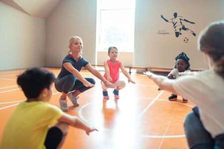 Taking exercises. School children bending their knees next to each other at their sports lesson.の写真素材