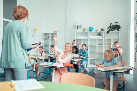 Maths class. Enthusiastic school children raising their hands doing sums with their maths teacher.