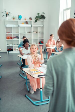 Answering tricky question. Enthusiastic school children raising hands to teachers question during the lesson.の写真素材