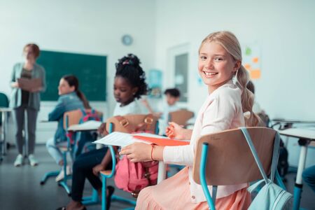 School friends. Cheerful school girl turning back to talk to her classmate during their maths lesson.の写真素材