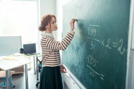 Preparing exercises. Beautiful concentrated teacher writing the task on the blackboard for her maths lesson.の写真素材