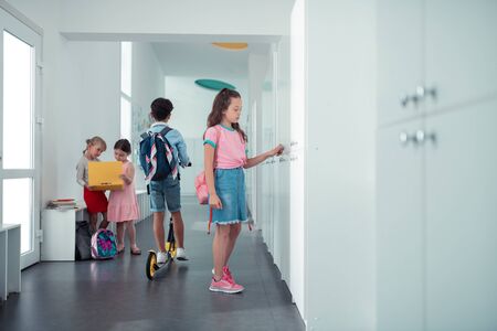 Girl near locker. Dark-haired schoolgirl wearing denim skirt and pink t-shirt standing near lockerの写真素材