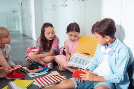 Discussing school schedule. Children discussing their school schedule during break while sitting near lockersの写真素材