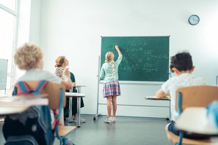 Counting in class. Smart school girl speaking and writing on a board in front oh the class.の写真素材