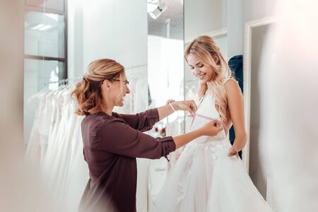 Designers workshop. Smiling tailor taking measures of a happy young woman in a wedding dress.の写真素材