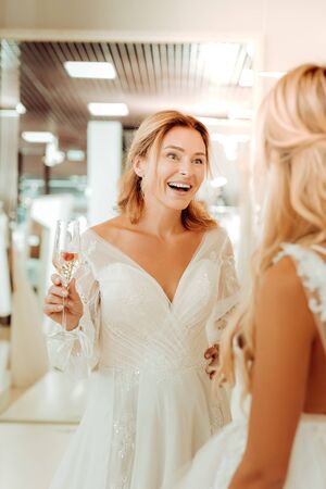Best shopping ever. Two happy brides drinking champagne with berries and talking in a wedding salon.の写真素材