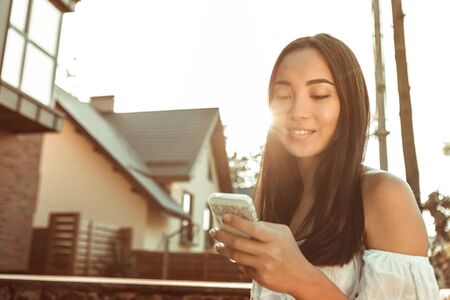 Beautiful girl. Pretty dark-haired woman with soft smile checking social media while staying in sunlightの写真素材