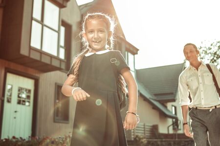 Daughter before school. Cute long-haired girl with wide smile wearing strict school uniform while going to schoolの写真素材