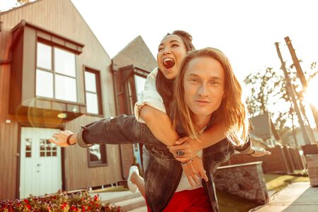 Spending funny date. Satisfied long-haired man in jacket having fun with pretty girl while staying in sunlightの写真素材