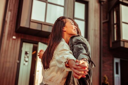 Great mood. Happy dark-haired girl being in love with strong boyfriend while tightly hugging himの写真素材