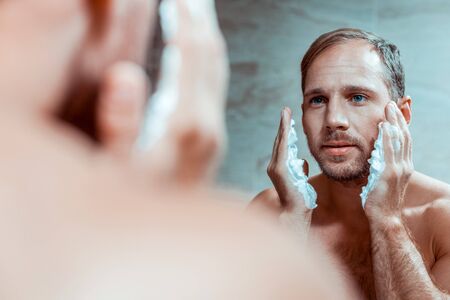 Attentive short-haired guy. Concentrated man having morning procedures in a bathroom before long working dayの写真素材