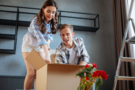 Couple unpacking box. Just married couple feeling excited while unpacking box while moving to new...