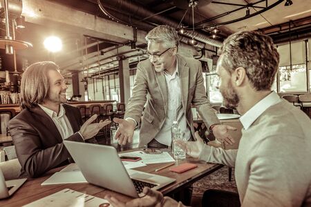 Best friends. Delighted longhaired man expressing positivity while talking to his colleagueの写真素材