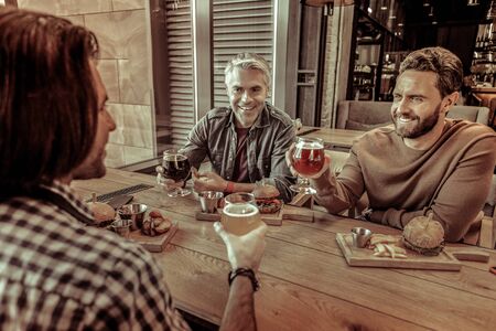 Dinner time. Joyful brunette keeping smile on his face while going to drink beerの写真素材