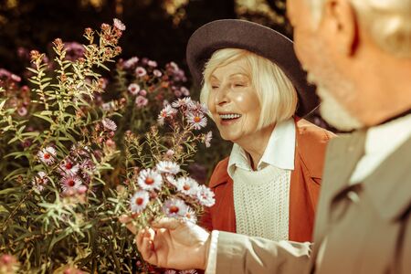 Smiling elderly lady and her husband leaning over beautiful flowers sniffing at them.